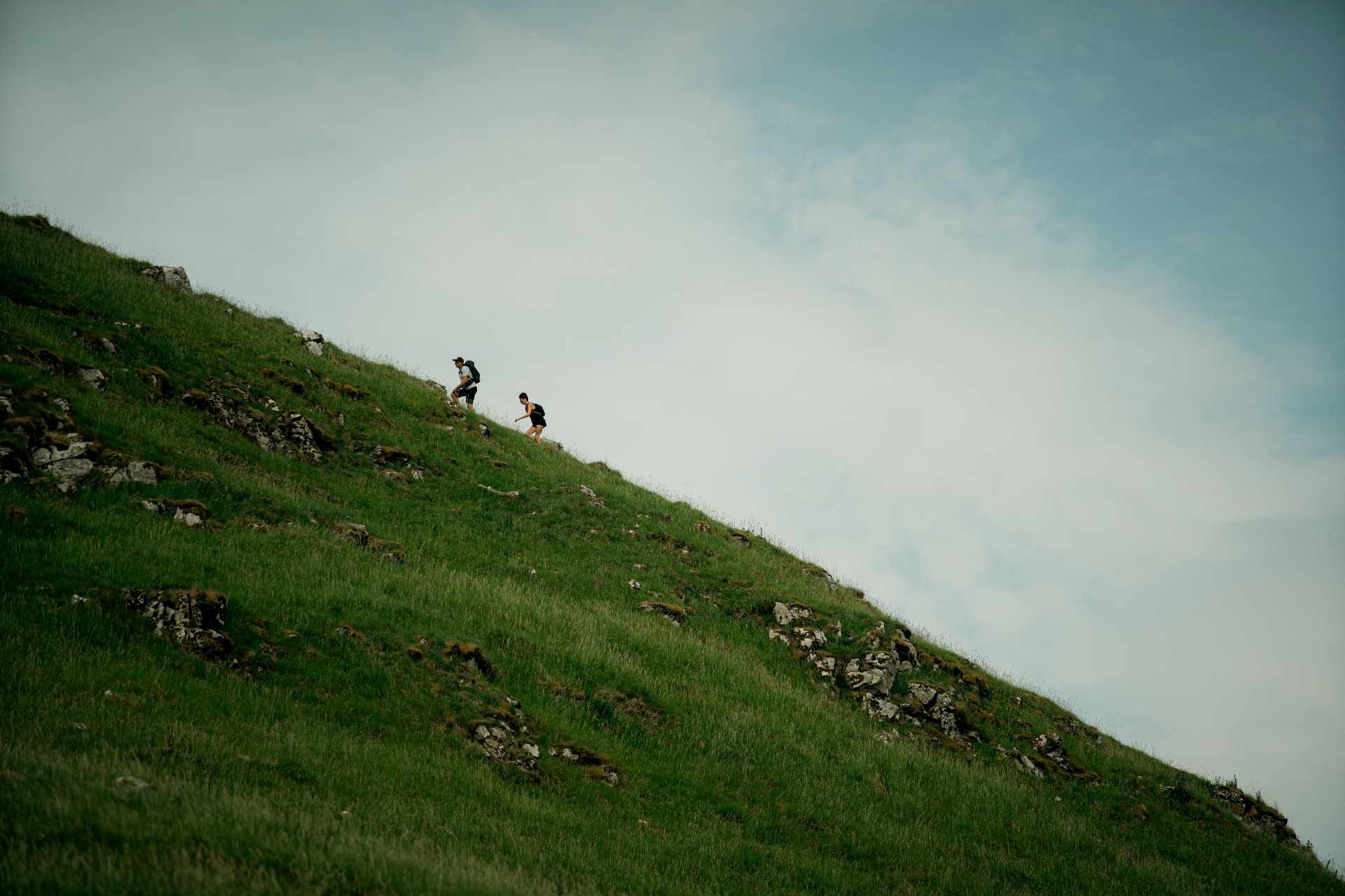 Two hikers ascending a grassy hillside under an open sky